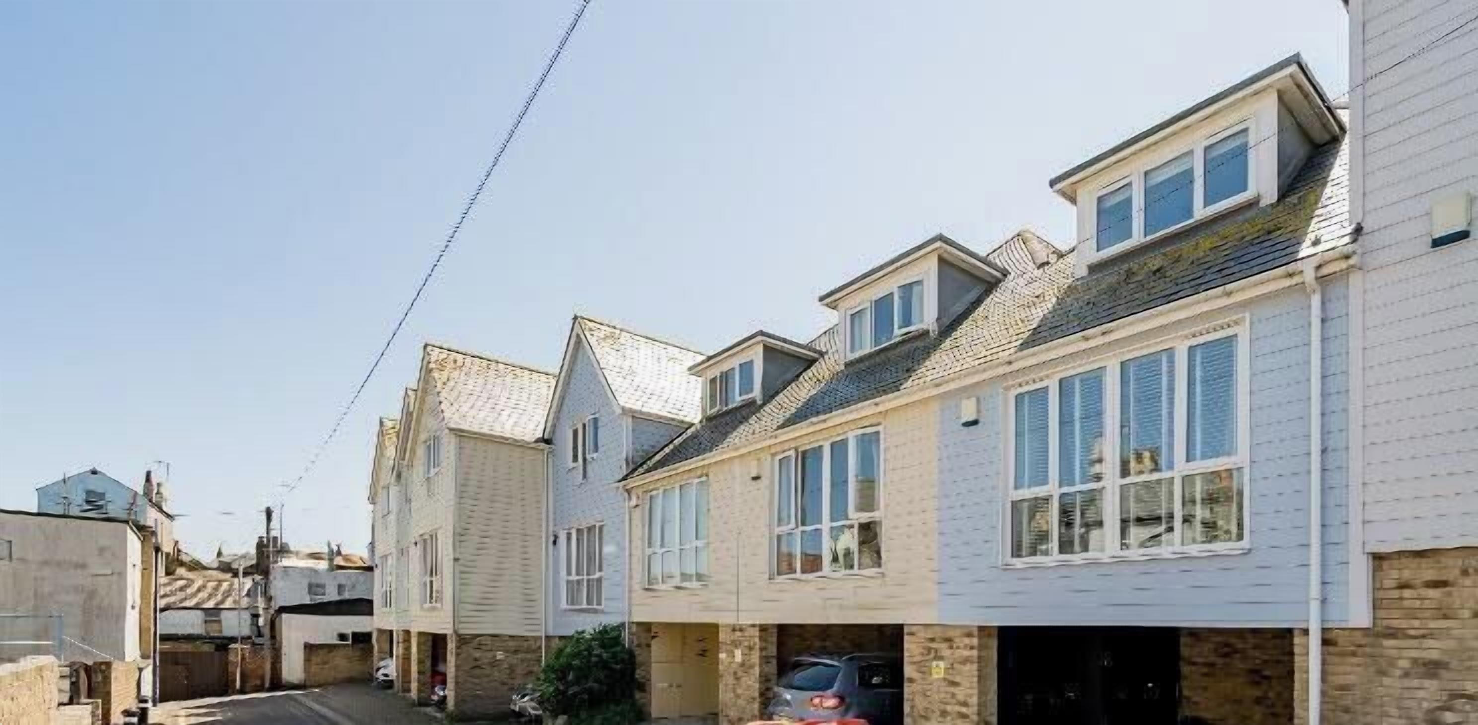 A row of townhouses with a narrow street, a parked car, and a clear sky.