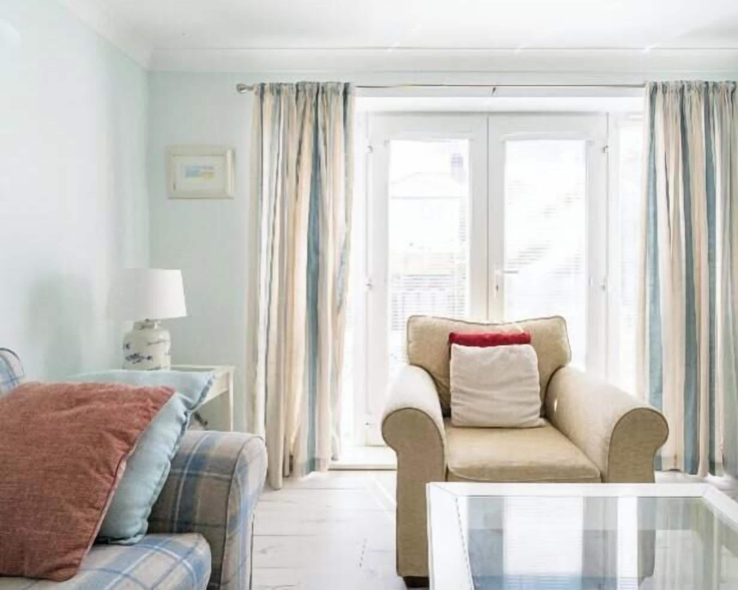 A room with a sofa, armchair, and a glass coffee table.