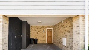 A narrow hallway with a black door on the left, a wooden door on the right, and a trash bin in the center. - Viking Bay House with Parking and Mins to Viking Bay Beach & Broadstairs Town (Broadstairs)