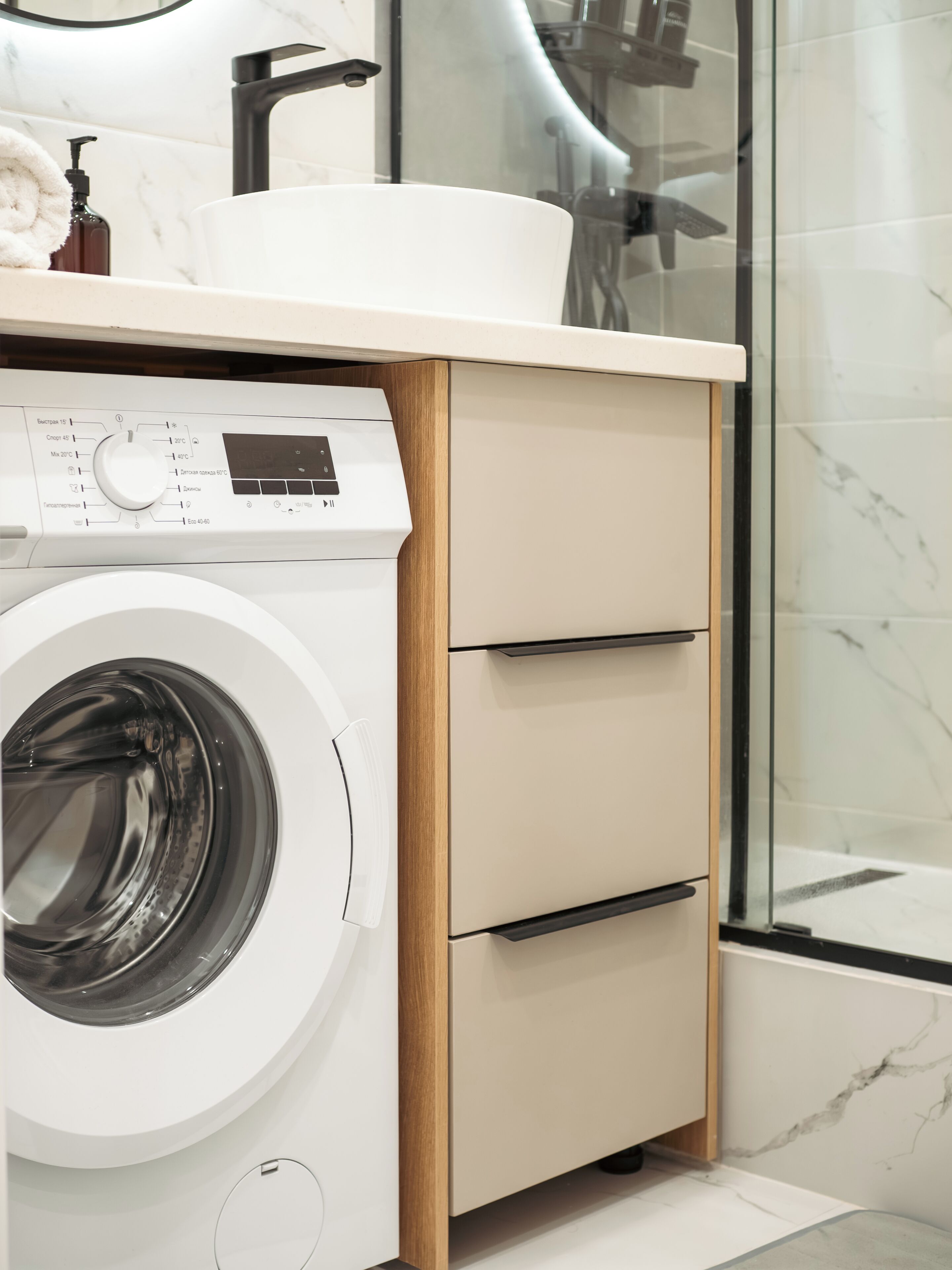 A modern bathroom with a washing machine, a sink, and a glass shower enclosure.