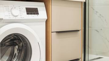 A modern bathroom with a washing machine, a sink, and a glass shower enclosure.