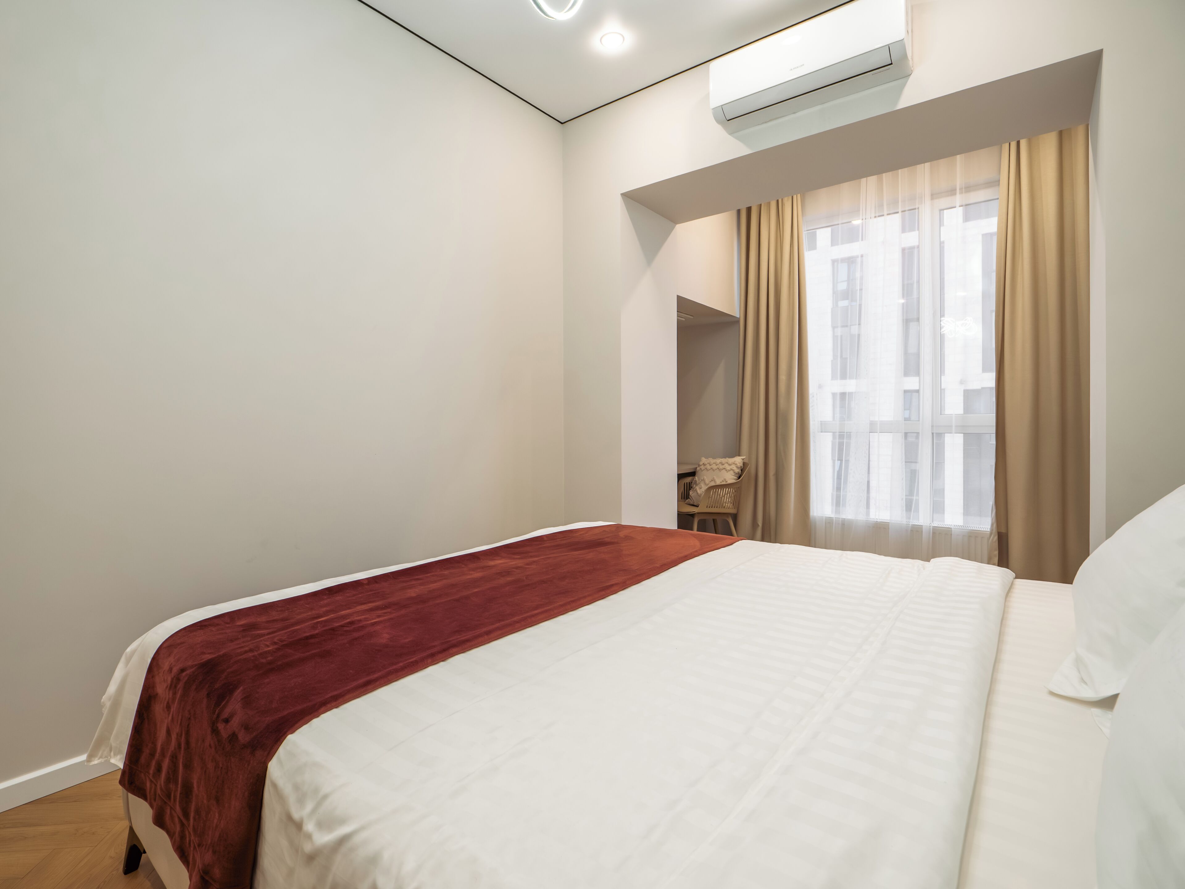A bedroom with a bed, a window with curtains, an air conditioning unit, and a chair.