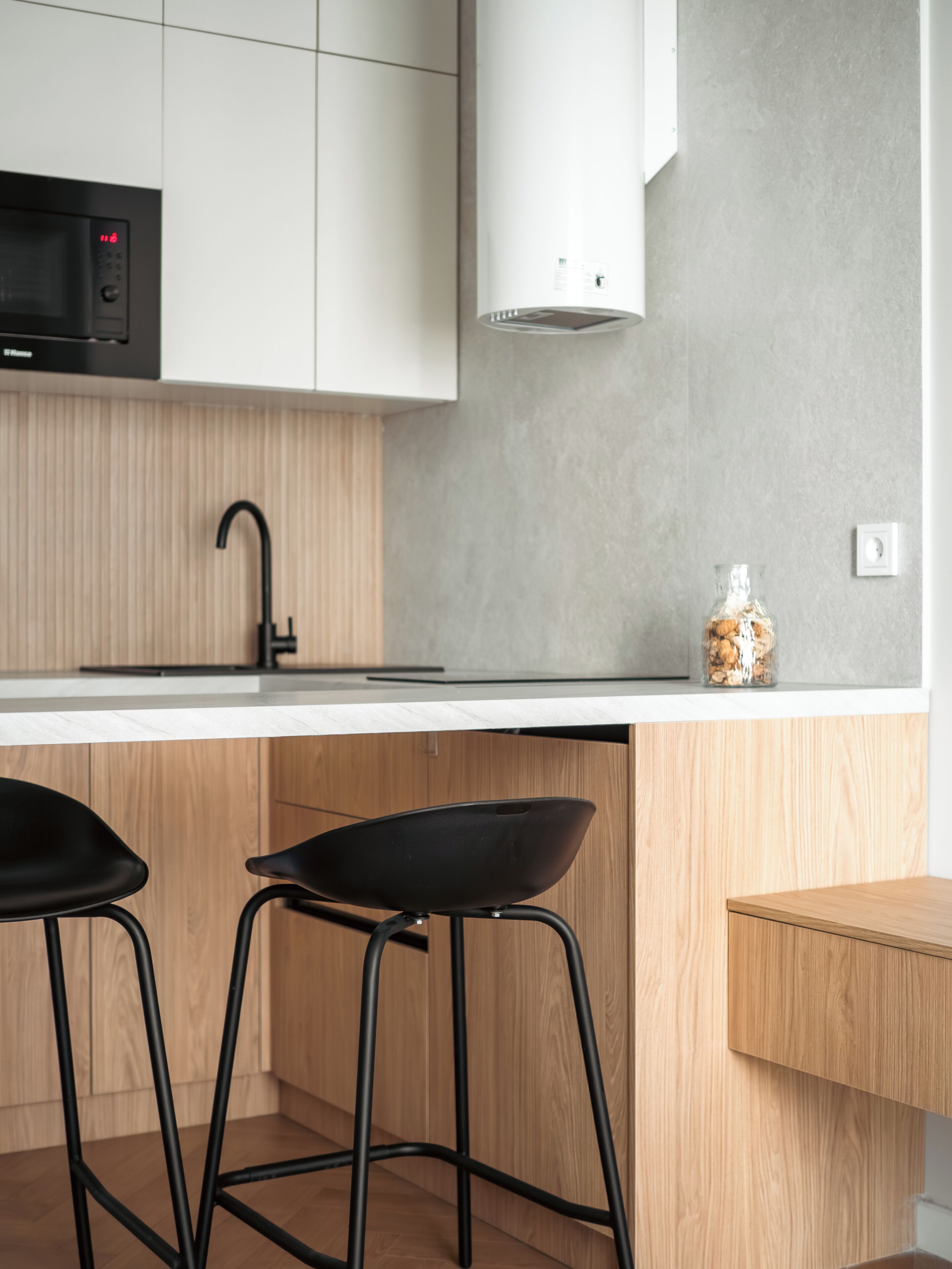 Una cucina moderna con un piano di lavoro bianco, sgabelli da bar neri, un lavello in acciaio inossidabile e un forno a microonde integrato.