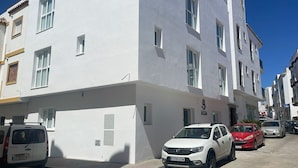 A multi-story building with a white facade, parked cars, and a clear blue sky. - AP Alsa 01 with Shared Terrace, WiFi, and Air Conditioning (Conil de la Frontera)