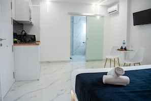 Ein modernes Hotelzimmer mit Bett, Schreibtisch, Stuhl und einem durch eine Glastür einsehbaren Badezimmer.
