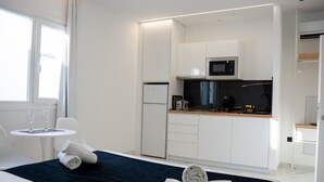 A modern hotel room with a bed, a small round table with two glasses, a dark blue bedspread, a neatly made white towel, a kitchenette with a microwave, a refrigerator, and a coffee maker. - AP Alsa 02 with Shared Terrace, WiFi, and Air Conditioning (Conil de la Frontera)