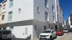 A multi-story building with a white facade, parked cars, and a clear blue sky. - AP Alsa 2.1 with Shared Terrace, WiFi and Air Conditioning (Conil de la Frontera)
