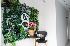 A reception area with a wall-mounted plant wall, a decorative letter, a small table with a basket of flowers, and a black chair. - AP Alsa 2.1 with Shared Terrace, WiFi and Air Conditioning (Conil de la Frontera)