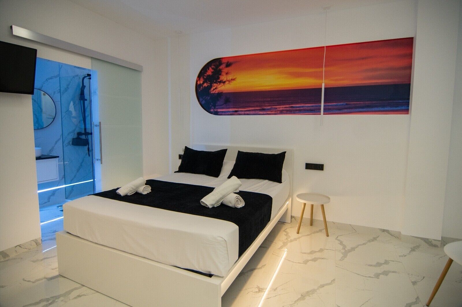 A modern bedroom with a bed, a nightstand, a painting, and a bathroom visible through a glass door.