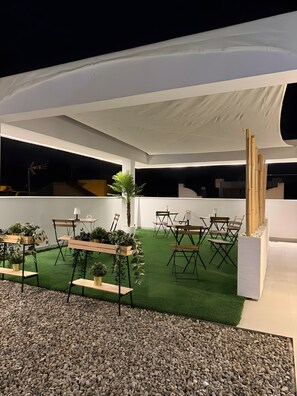 An outdoor event space with a white tent, green artificial turf, wooden tables with chairs, and potted plants. - AP Alsa 2.1 with Shared Terrace, WiFi and Air Conditioning (Conil de la Frontera)