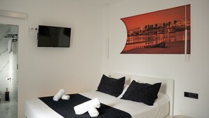 Una moderna camera d'albergo con un letto, una televisione a schermo piatto, un'ampia cornice con un'immagine e un bagno con rivestimento in marmo.