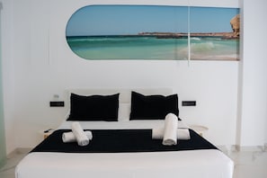 A bed with two black pillows, a white bedspread, and two rolled towels.