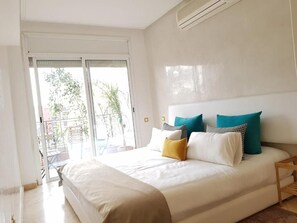 A bedroom with a bed, pillows, a nightstand, and a sliding glass door leading to an outdoor area. - Urban Chic 2 bedrooms in  City Center (Marrakesh)