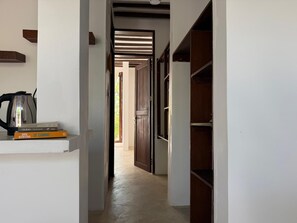 Um corredor com uma cafeteira, livros e uma porta de madeira que dá para outro quarto.