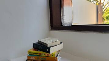 A stack of books on a white surface near a window with a clear view of a tree outside.