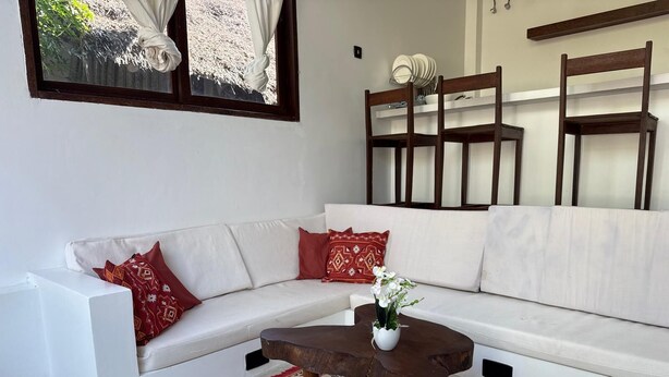 Ein stilvolles Wohnzimmer mit einem weißen Sofa, roten Kissen, einem Holztisch und einem gemusterten Teppich.