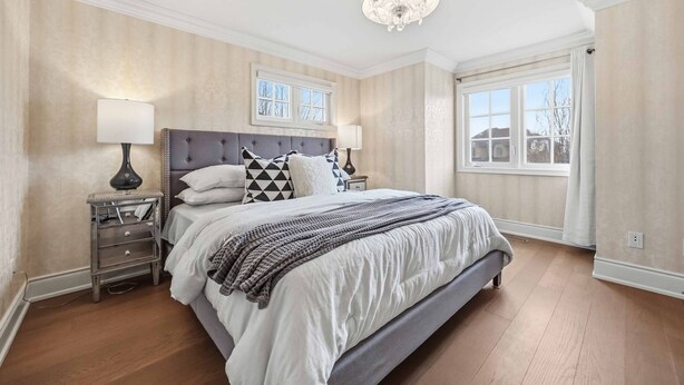 A bedroom with a large bed, two bedside tables, a chandelier, and a window with curtains.