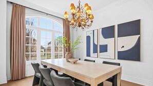 A dining area with a large table, chairs, a chandelier, and artwork on the wall.