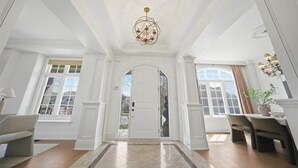 A spacious entryway with a grand chandelier, a white door, and a dining area with chairs and a table.