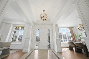 A spacious entryway with a grand chandelier, a white door, and a dining area with chairs and a table.