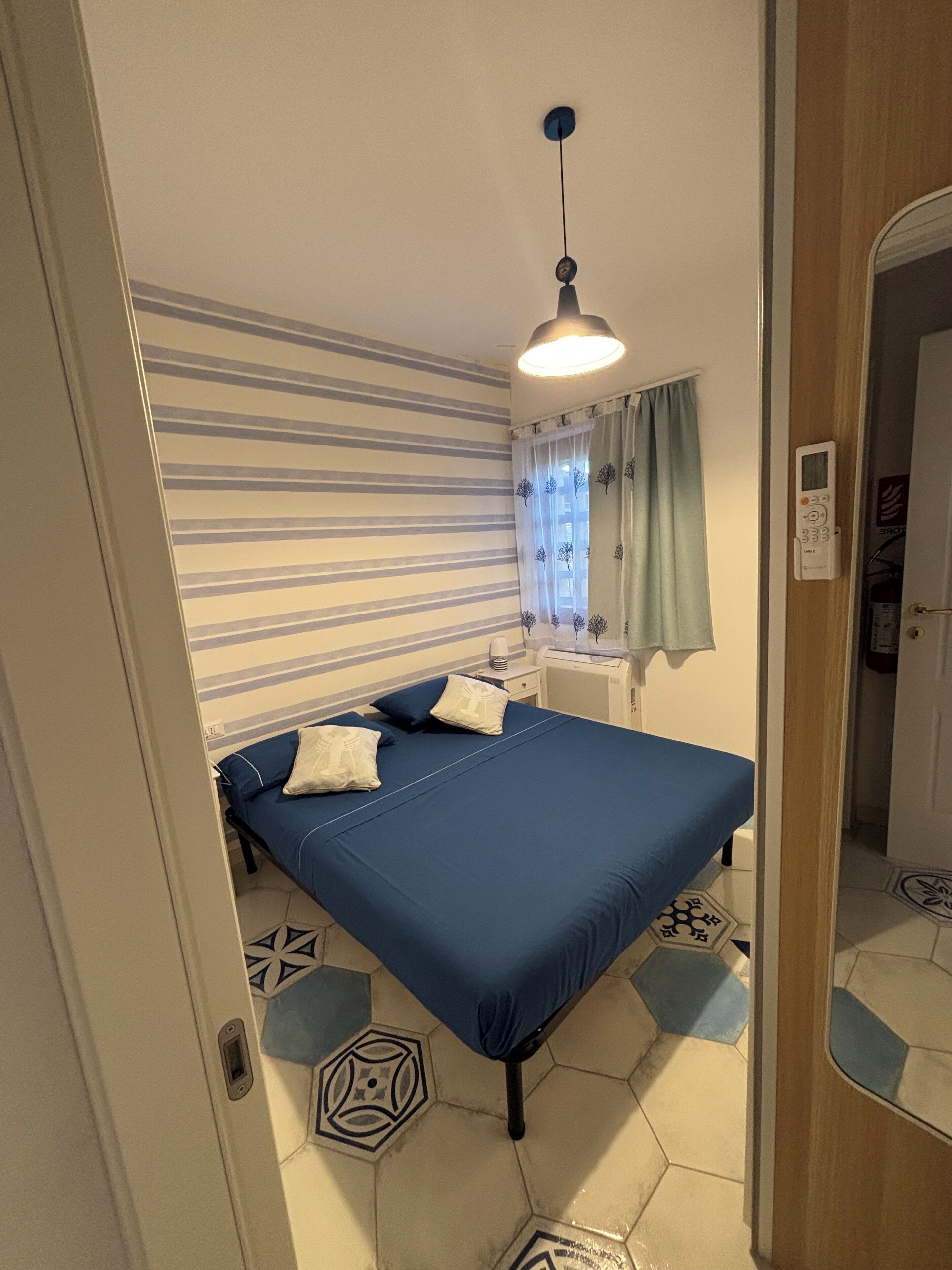 A bedroom with a bed, a nightstand, a lamp, a window with curtains, and a door.