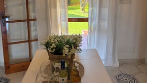 A hotel room with a view of a garden, a table with a tray of amenities, a clock on the wall, and a decorative ceiling light. - Le Tonnare 36 (Sardegna)