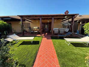 Un patio con sendero de ladrillo rojo, mobiliario exterior y un área de estar cubierta.