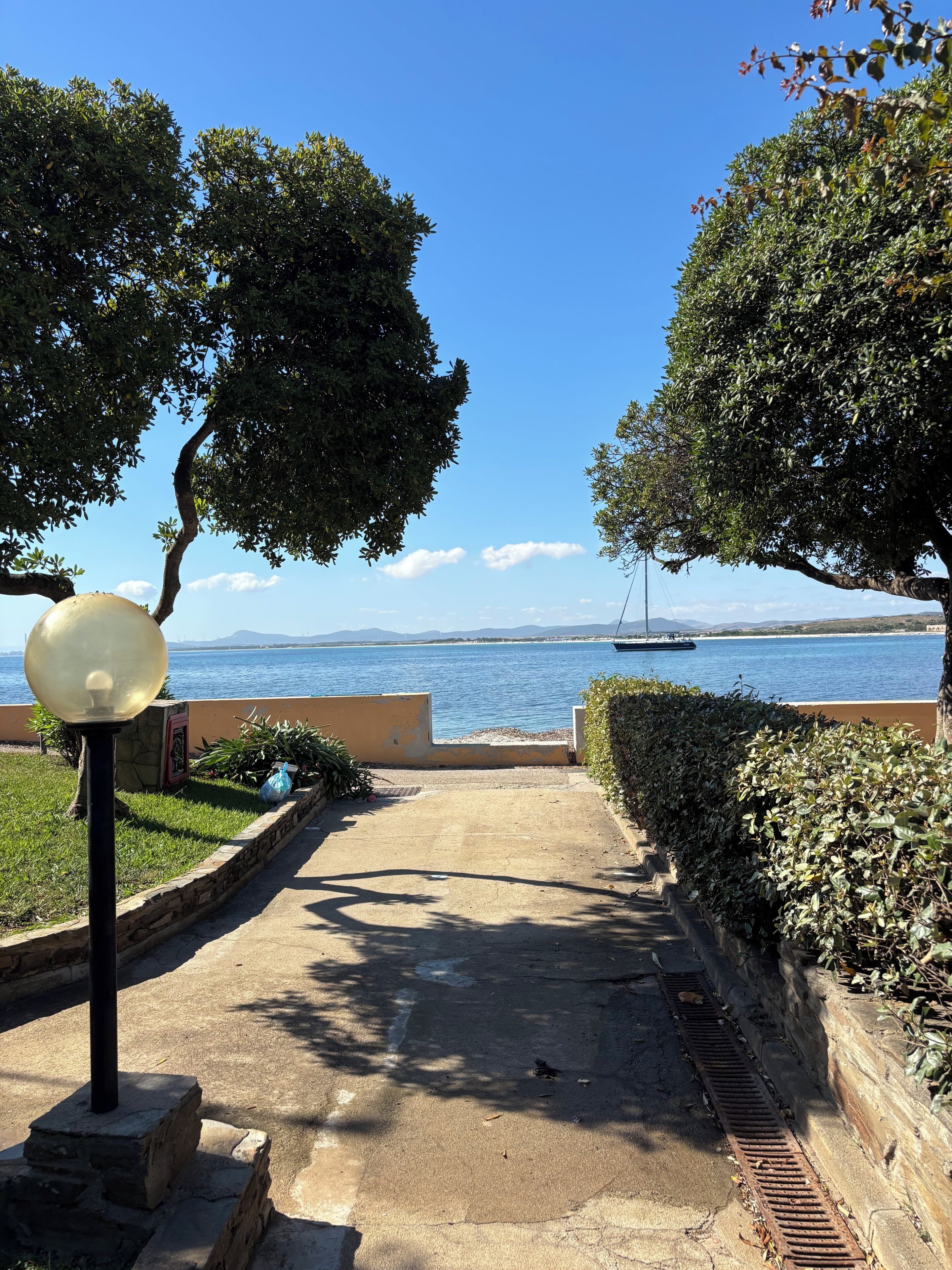 A pathway leading to a body of water with a sailboat visible in the distance.