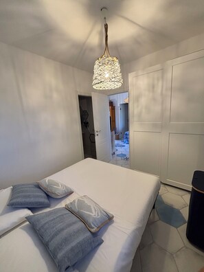 Ein Schlafzimmer mit Bett, Kissen, einer Pendelleuchte und einer Tür zu einem Badezimmer.