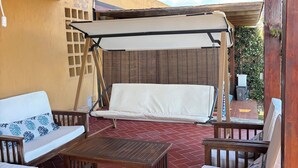 A covered outdoor seating area with a wooden table, chairs, and a swing. - Le Tonnare 36 (Sardegna)