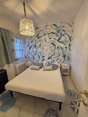 A bedroom with a bed, nightstands, a wall mural, and a hanging light fixture.
