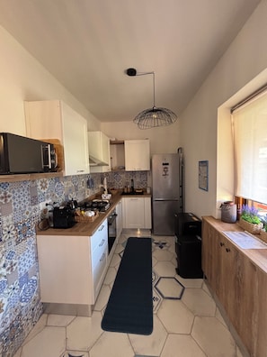 A kitchen with a microwave, stove, refrigerator, and a hanging light fixture.