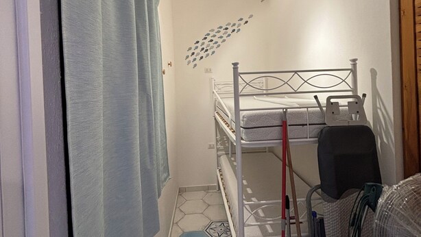 A small, compact room with a bunk bed, a shower curtain, a wall-mounted fan, and a patterned floor. - Le Tonnare 36 (Sardegna)