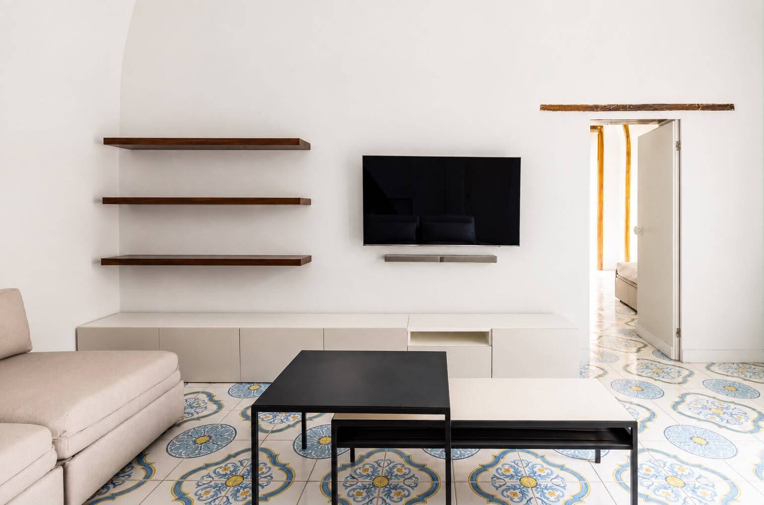 A living room with a sofa, a coffee table, a TV mounted on the wall, and a patterned floor.