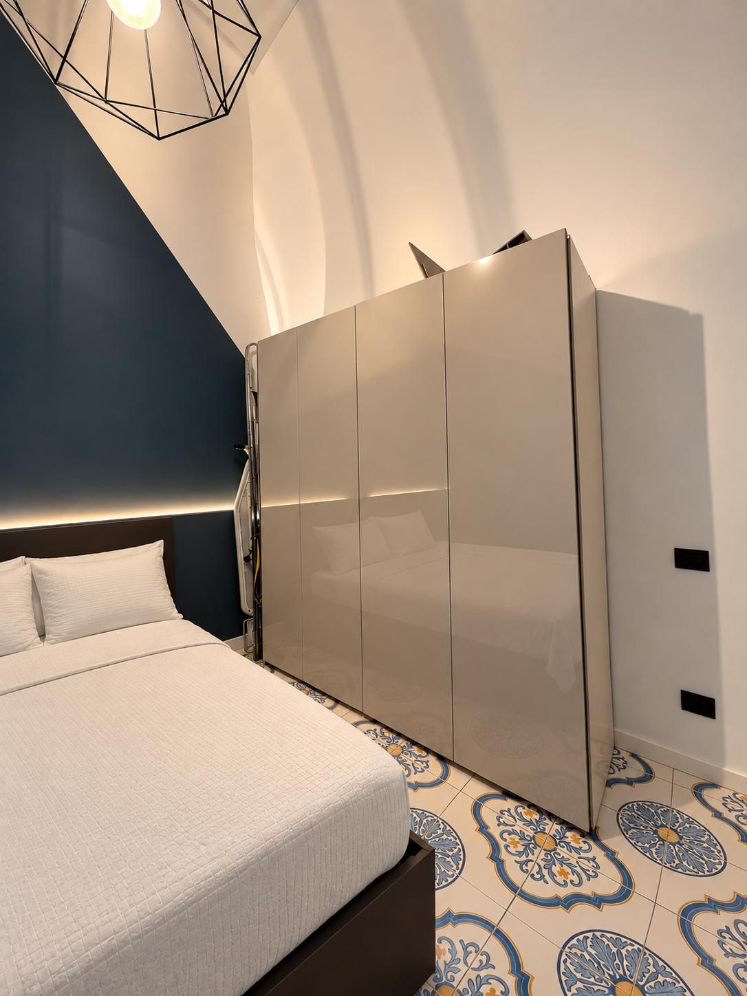 A bedroom with a bed, a wardrobe, and a geometric light fixture.