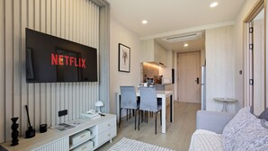 A modern living room with a flat-screen TV mounted on the wall, a dining area with a table and chairs, and a kitchen in the background. - Bangtao Laguna Apartment 42 sq.m (Thalang District)
