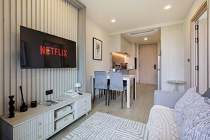 Ein modernes Wohnzimmer mit Wand-Fernseher, einem Essbereich mit Tisch und Stühlen sowie einer Küche im Hintergrund.