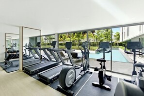 Ein modernes Fitnessstudio mit Laufbändern, Crosstrainern und Blick auf einen Pool.
