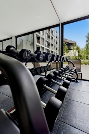 Ein Fitnessstudio mit Reihen von Kurzhanteln und Langhanteln, großen Fenstern und Blick auf ein Gebäude.