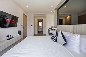 Ein modernes Hotelzimmer mit einem großen Bett, einem Schreibtisch, einem Sessel und einem an der Wand befestigten Fernseher.