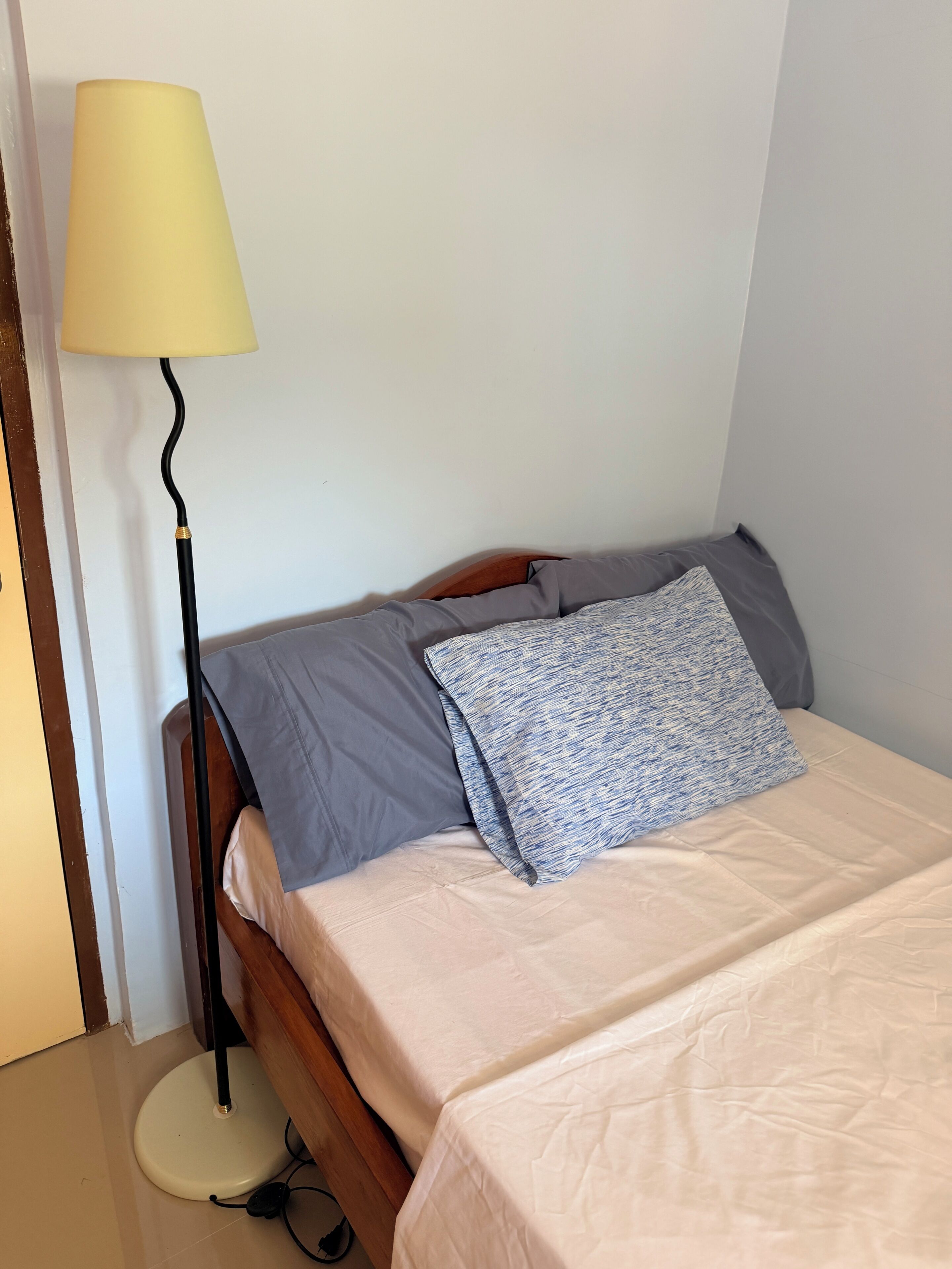 En säng för en person med en träram, ett sängbord, en lampa och en prydd kudde.