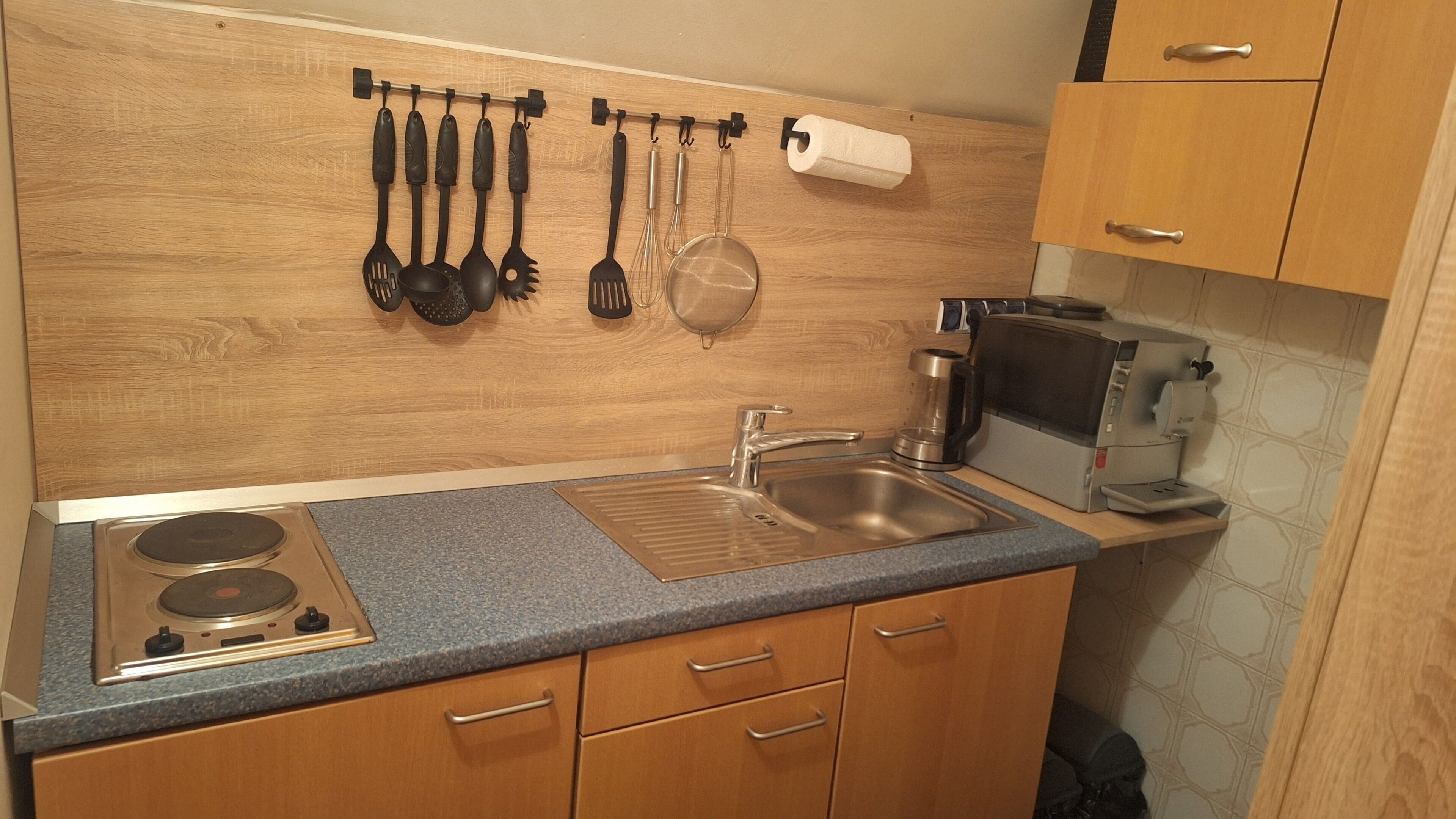 A kitchen with a stainless steel sink, wooden cabinets, a built-in stove, and various utensils hanging on the wall.