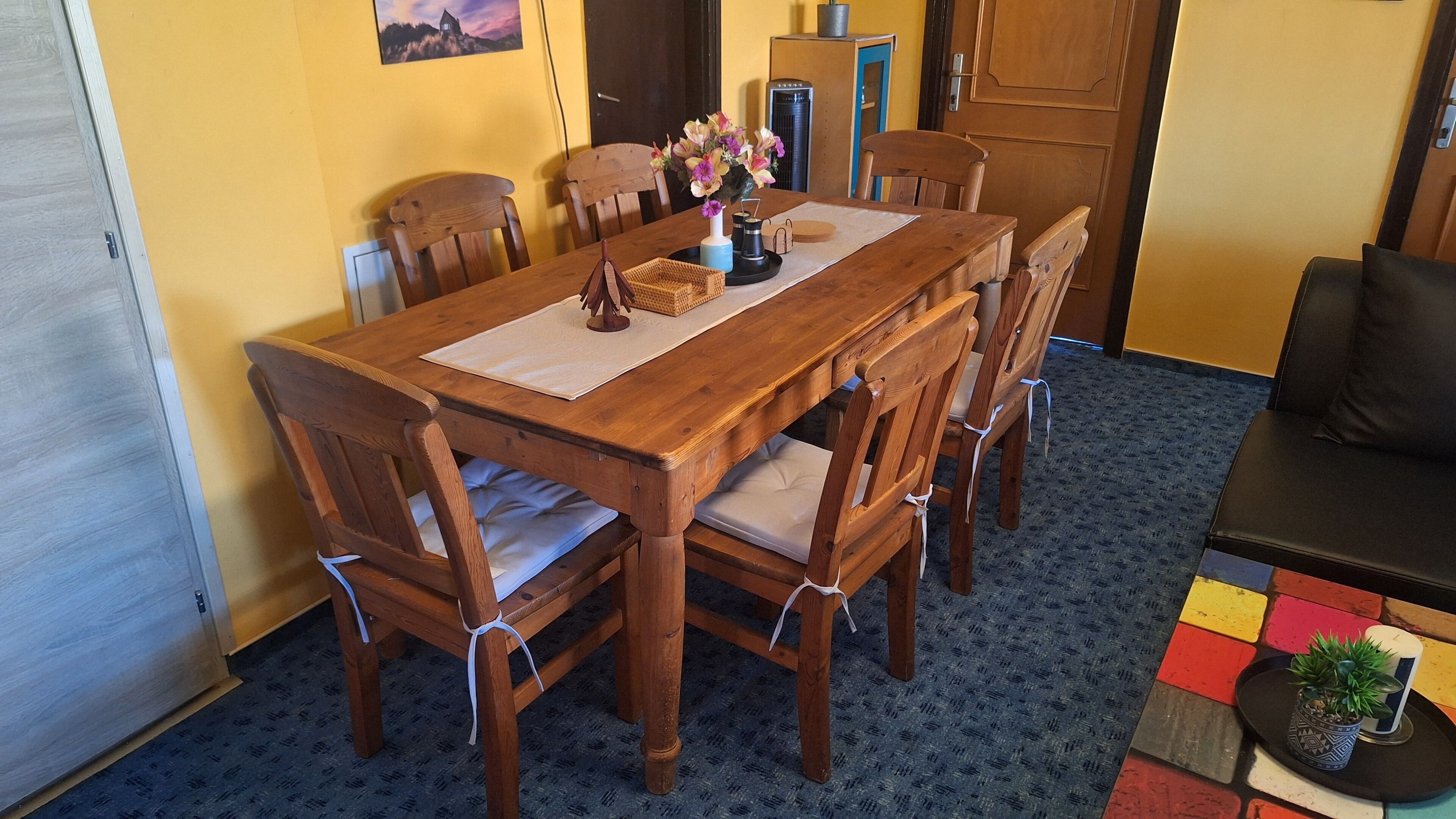 Una mesa de comedor de madera con seis sillas, un jarrón con flores y una pequeña cesta.