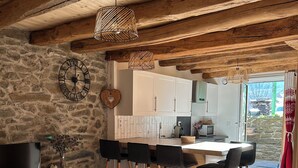 A rustic interior with a stone wall, wooden furniture, a dining area with chairs, a television, and a kitchen visible through an open door. - Apartment with Balconies (sleeps 6) (Saint-Michel-de-Maurienne)
