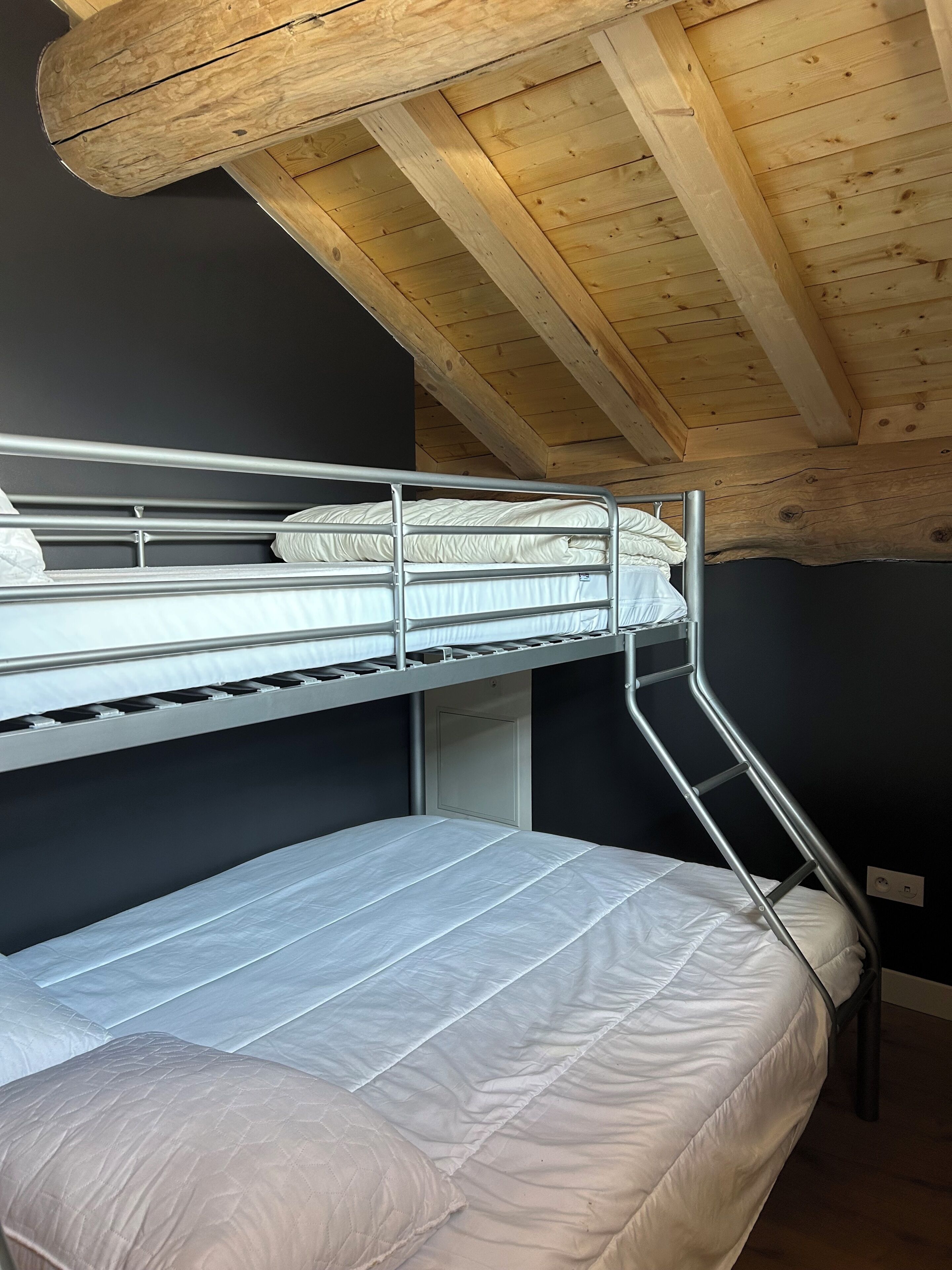 Un lit superposé avec un escalier en métal, un lit inférieur avec un matelas et un plafond en bois.