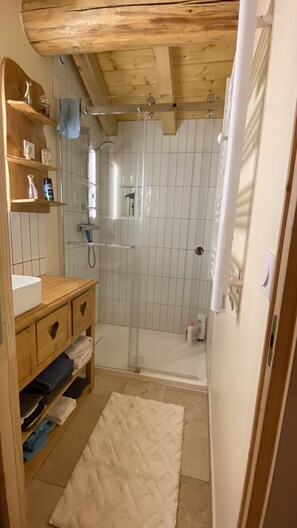 A bathroom with a wooden vanity, a glass shower enclosure, and a white rug on the floor. - Apartment with Balconies (sleeps 6) (Saint-Michel-de-Maurienne)