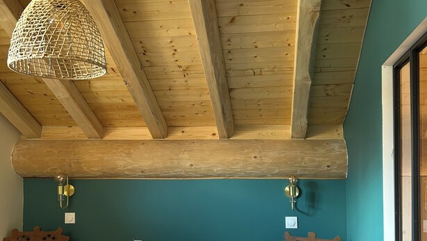 A bedroom with a wooden ceiling, a bed with white bedding, a woven light fixture, and a wall-mounted clock. - Apartment with Balconies (sleeps 6) (Saint-Michel-de-Maurienne)