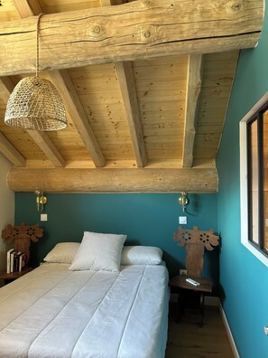 A bedroom with a wooden ceiling, a bed with white bedding, a woven light fixture, and a wall-mounted clock. - Apartment with Balconies (sleeps 6) (Saint-Michel-de-Maurienne)