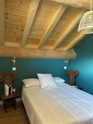 A bedroom with a wooden ceiling, a bed with white bedding, and a wall-mounted light fixture. - Apartment with balconies (sleeps 6) (Saint-Michel-de-Maurienne)