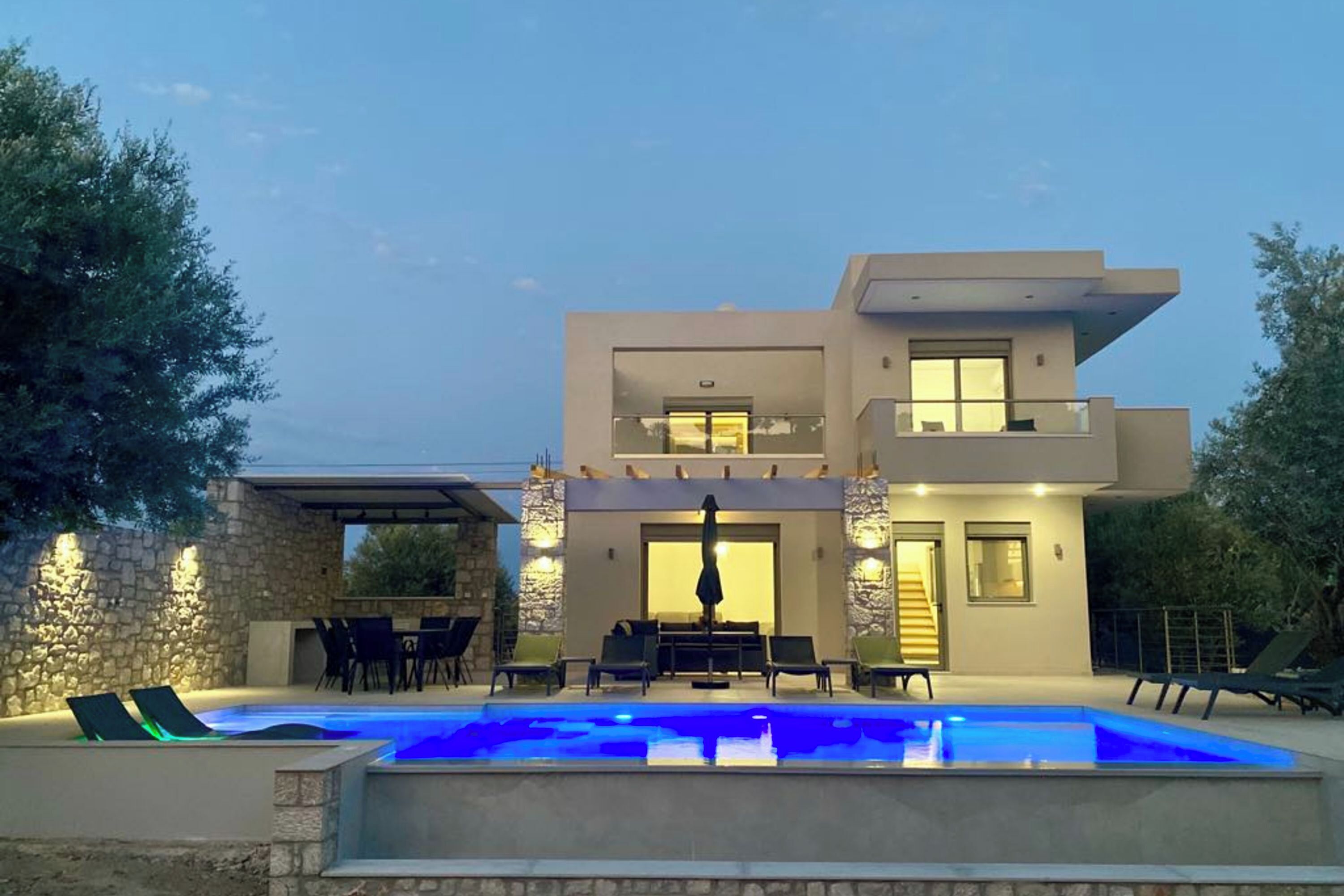 A modern two-story house with a swimming pool, outdoor seating, and a stone wall.